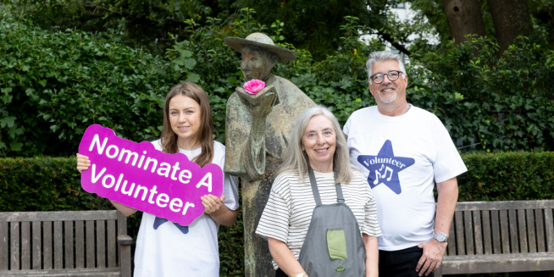 three smiling volunteers pose with a statue
